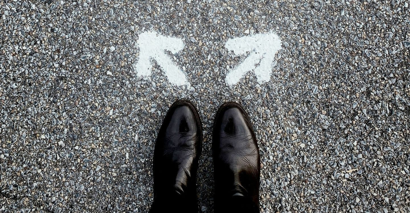 A pair of shoes in front of two arrows painted on the asphalt, pointing in different directions.