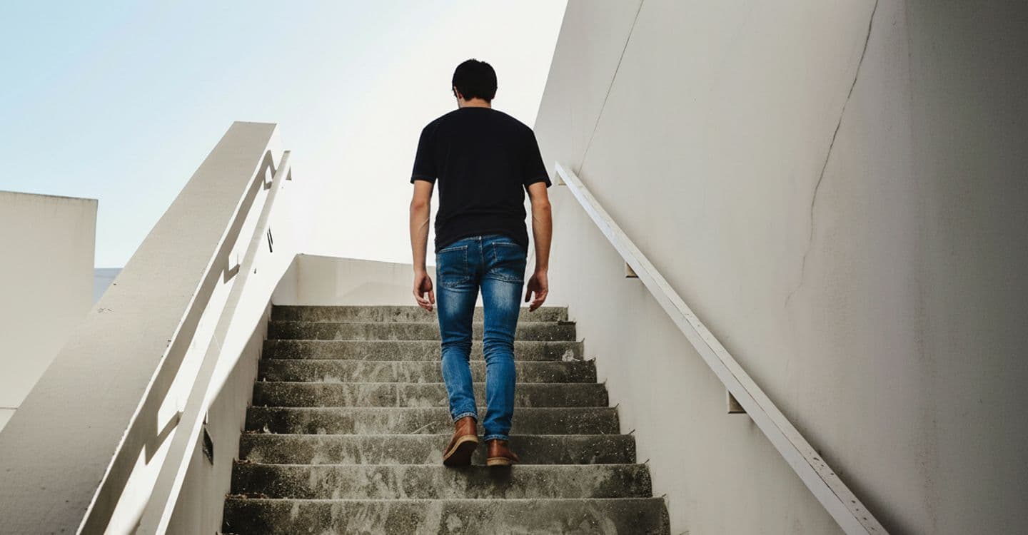 A man climbing a flight of stairs towards the light.